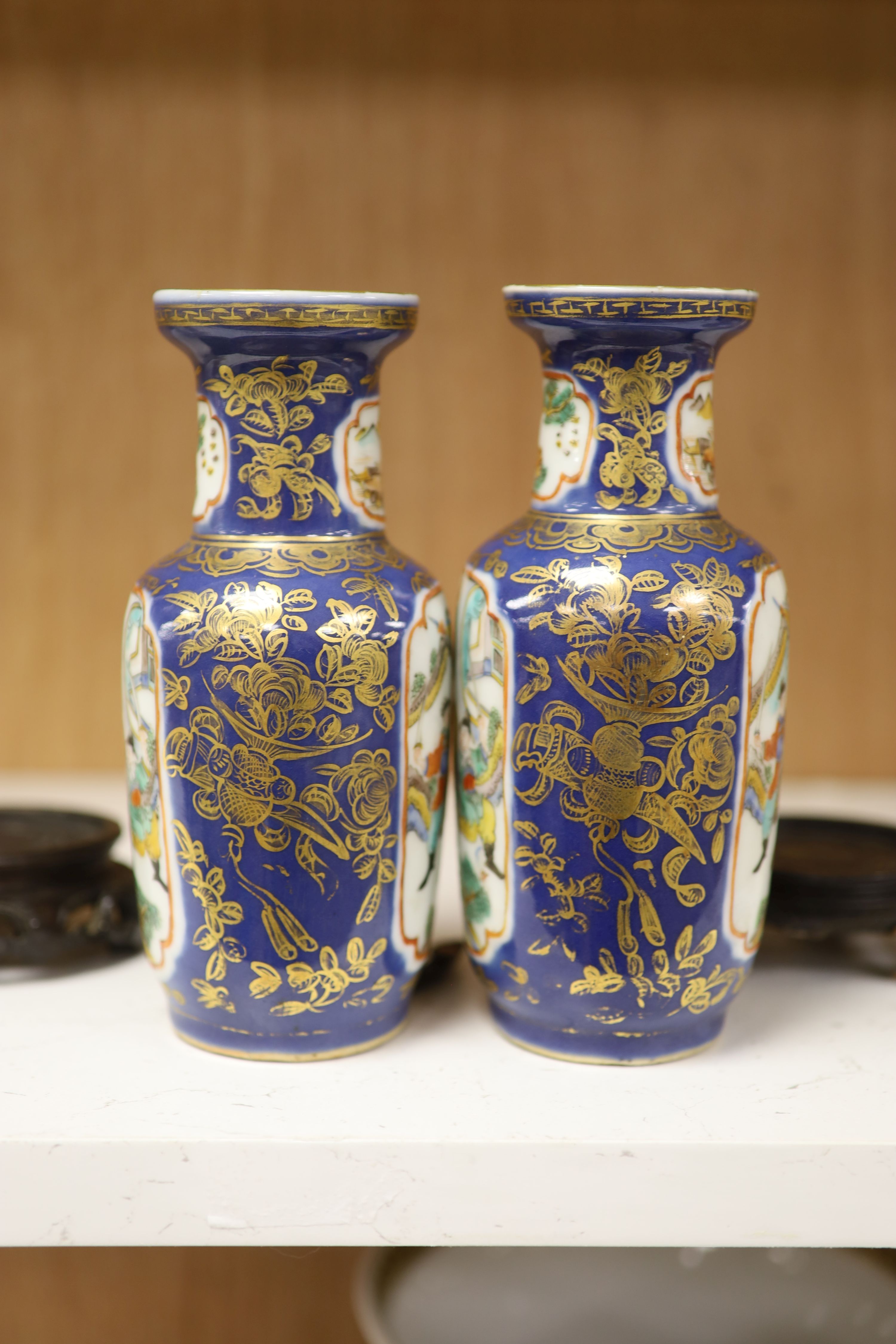 A pair of Chinese Kangxi style blue-ground vases, late 19th century decorated with panels of warriors and heightened in gilt, on carved hardwood stands, height 18cm excluding stand